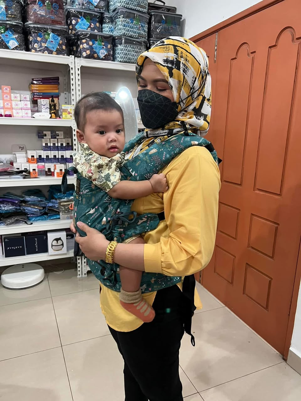 Ibu memakai baby carrier bercorak hijau bersama bayinya